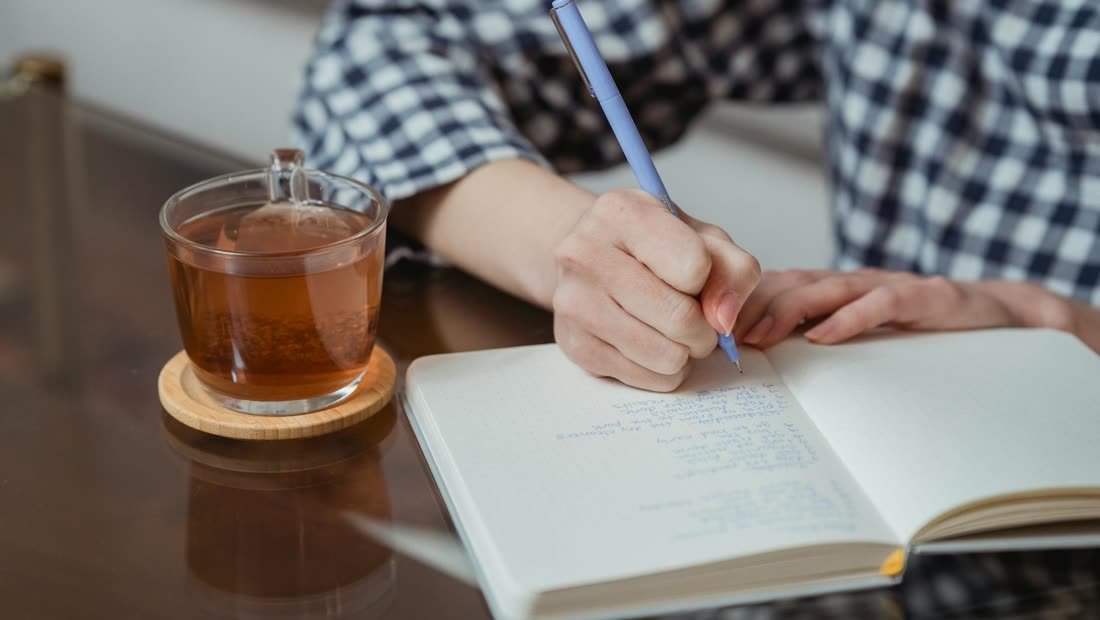Hands writing in a notebook beside tea, tracking progress through the second smoke-free day